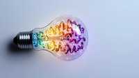 Colorful rainbow brain-shaped filament glowing inside clear light bulb on gray background, symbolizing creative thinking and innovation.