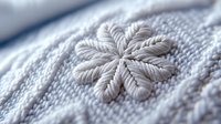 Delicate white embroidered snowflake pattern on soft knitted fabric, extreme close up macro photography showing detailed texture and craftsmanship of winter clothing.