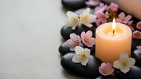 Spa wellness concept with burning candle, black hot stones and delicate cherry blossom flowers arranged for relaxation and meditation therapy treatment.