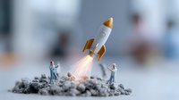 Miniature astronauts on moon-like surface observe white rocket launch with orange nose cone and flame exhaust, creative business concept setup on gray terrain.
