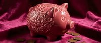 Decorative pink ceramic piggy bank with ornate floral patterns sits on luxurious purple velvet fabric with scattered coins for savings and financial planning.