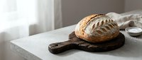 Freshly baked artisan sourdough bread loaf on wooden cutting board in modern kitchen counter, natural lighting for bakery and food photography.