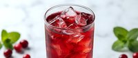Refreshing cranberry juice cocktail with ice cubes in a glass, garnished with fresh mint and berries on a marble background.
