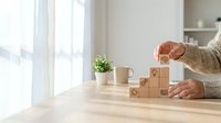 Hand arranging wooden blocks with business icons in staircase formation on desk, symbolizing strategy, growth, and step-by-step planning.