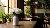 White hydrangea flowers in ceramic vase on rustic wooden table with fern plants in cozy kitchen interior with natural sunlight streaming through windows.