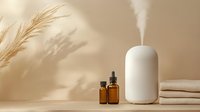 Minimalist spa wellness setup with white aromatherapy diffuser releasing steam, amber essential oil bottles and soft towels on neutral background.