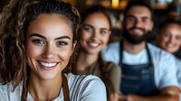 Diverse group of young cafe workers smiling at camera, wearing aprons and casual attire. Friendly service staff portrait showing teamwork and positive workplace atmosphere.