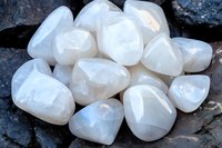 Polished white moonstone crystals on dark rock background, displaying natural iridescence and adularescence. Healing stones for spiritual practices.