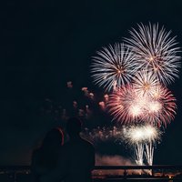 Couple silhouettes watching spectacular fireworks display over water at night. Romantic celebration scene for holidays, New Year, Fourth of July events.