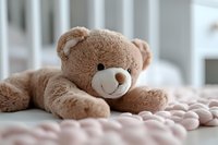 Soft brown teddy bear lying on pink knitted blanket, close-up view with shallow depth of field creating dreamy nursery atmosphere for childhood and baby concepts.