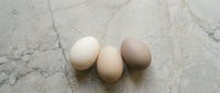 Four fresh brown chicken eggs arranged on elegant marble countertop surface for cooking and baking recipes in modern kitchen setting.