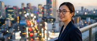 Young Asian businesswoman in glasses smiling on city rooftop terrace at dusk with urban skyline and lights background for corporate success concepts.