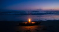 Glowing lantern on sandy beach at twilight with ocean waves and purple sunset sky creating peaceful coastal atmosphere for meditation and relaxation.