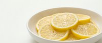 Fresh lemon slices arranged in a white ceramic bowl on a light background, showcasing vibrant yellow citrus fruit for food and beverage concepts.