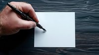 Hand holding black pen over blank white paper on dark wooden table background, ready for writing or creative work. Minimalist composition for business concept.