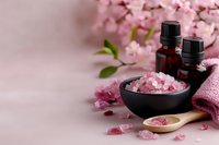 Pink cherry blossom spa setting with essential oil bottles, bath salt in wooden spoon and bowl, towel for aromatherapy wellness relaxation treatment.