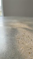 Low angle view of polished concrete floor with aggregate texture in empty interior space with natural light from window and neutral walls.