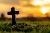 Stone cross on grassy ground at sunset with golden sky and sun in background, creating spiritual atmosphere for religious and memorial concepts.