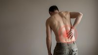 Young athletic man experiencing lower back pain holding spine area with red inflammation highlight showing muscle strain injury and discomfort needing treatment.