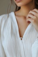 Close-up portrait of young Asian woman in white pleated blouse showing delicate neckline, natural makeup, and manicured hands for fashion and beauty advertising.