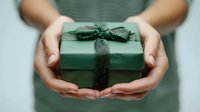 Female hands holding green gift box with ribbon bow for holiday celebration and special occasions.