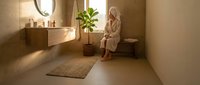 Young blonde woman in bathrobe relaxing in modern luxury bathroom with wooden vanity, round mirror and plant for spa wellness interior design.