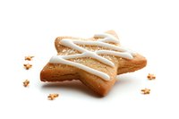 Star-shaped sugar cookie with white icing drizzle on isolated white background, surrounded by cookie crumbs. Fresh baked holiday treat for festive occasions.