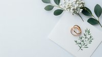 Elegant wedding invitation with gold rings and eucalyptus branches on white background, styled for romantic celebration.