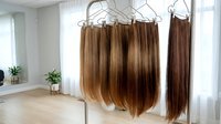 Professional hair extensions hanging on display hangers in modern salon interior, showcasing various brown and blonde color options for hairstyling services.