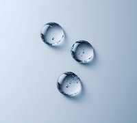 Clear water drops on light surface create minimalist composition with natural refraction and shadows, showing purity and freshness in macro photography.