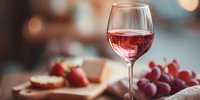Elegant wine glass filled with red wine alongside fresh grapes and cheese platter creating sophisticated dining atmosphere for restaurant menus and culinary content.