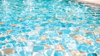 Rippling turquoise swimming pool water surface with sunlight reflections creating dynamic patterns and abstract aqua textures with golden highlights.