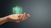 Hand holding glowing green cybersecurity shield with wifi and lock symbols representing digital protection and network security technology.