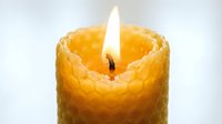 Burning beeswax candle with honeycomb texture, warm golden flame glowing against light background, natural eco-friendly home decor.