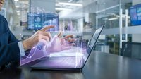 Businessman in blue suit analyzing financial data with holographic charts and graphs emerging from laptop screen in modern office environment.