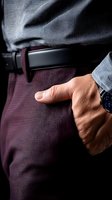 Close-up of male hand in pocket wearing formal burgundy striped trousers, black leather belt, and blue dress shirt sleeve with wristwatch, showing business attire detail.