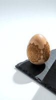 Wooden egg with intricate mandala patterns engraved on surface, displayed on dark slate board against clean white background for Easter decoration.
