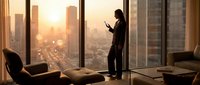 Young professional woman in business attire standing by floor-to-ceiling windows in high-rise office, holding tablet, overlooking golden sunset cityscape. Corporate workspace concept.