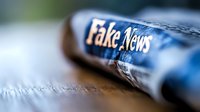 Rolled newspaper with text visible on blue tinted paper, shallow depth of field macro photography showing media and journalism concept in dramatic lighting.