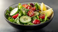 Fresh garden salad with sliced cucumber, cherry tomatoes, mixed greens and sesame seeds served in black ceramic bowl on dark background. Healthy meal.