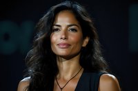 Professional Hispanic woman with curly dark hair smiling confidently in business attire against blurred background for corporate presentations.