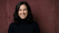 Professional Hispanic businesswoman with curly hair smiling confidently in black turtleneck against burgundy background for corporate headshots and marketing.