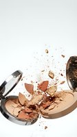 Broken makeup powder compact with scattered fragments and dust particles on white background for beauty and cosmetics design projects.