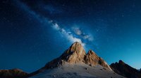 Majestic mountain peak under starry night sky with bright Milky Way galaxy stretching across deep blue space, dramatic natural landscape photography.