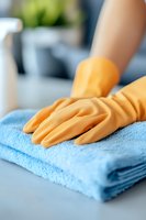 Person wearing yellow rubber gloves wiping blue microfiber cloth on clean surface, representing household cleaning and hygiene maintenance.