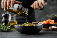 Pouring olive oil over fresh salad in black ceramic bowl on dark background, with herbs and ingredients. Food preparation process in moody lighting.