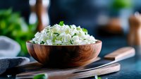 Freshly cooked white rice garnished with chopped green herbs in wooden bowl, served on dark background with chopsticks. Asian cuisine food styling.