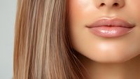 Close up view of plump glossy lips and straight blonde hair against neutral background, showcasing natural beauty makeup and skincare results.