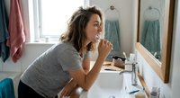 Young Caucasian woman brushing teeth in modern bathroom mirror reflection morning routine dental hygiene self-care wellness lifestyle.