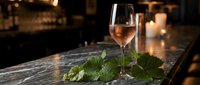 Glass of rosé wine with fresh mint leaves on marble bar counter in upscale restaurant setting with warm ambient lighting for hospitality and dining concepts.